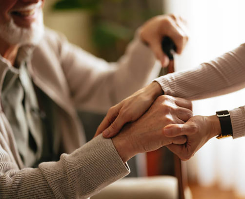 Unrecognizable Japanese female caregiver supporting her smiling elderly patient to stand up.